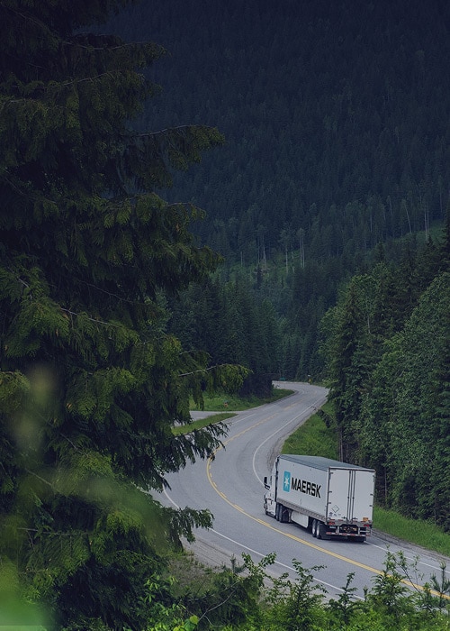 Maersk truck transporting cargo through scenic forest route, highlighting sustainable road freight logistics solutions