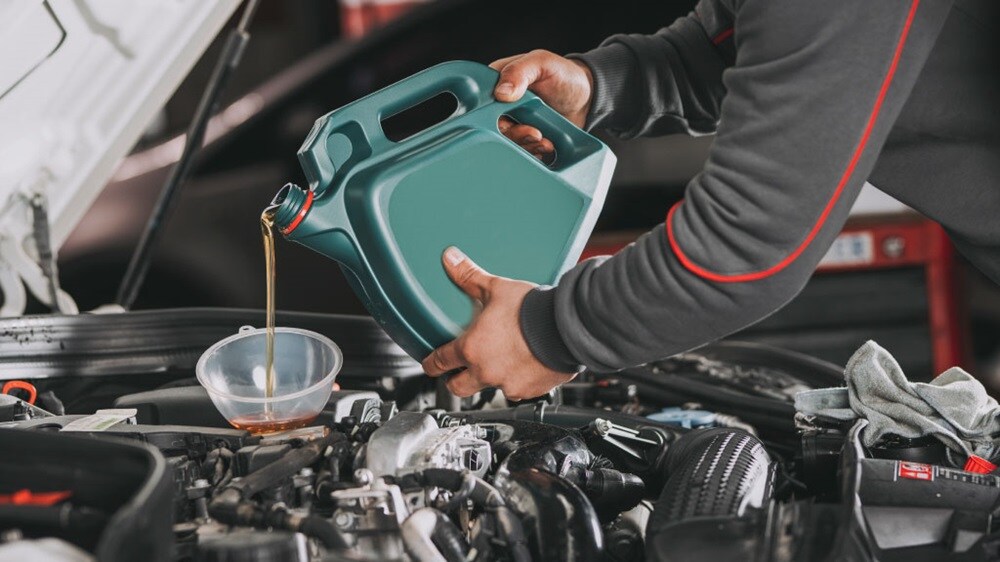 A set of hands pouring chemical lubricant into engine